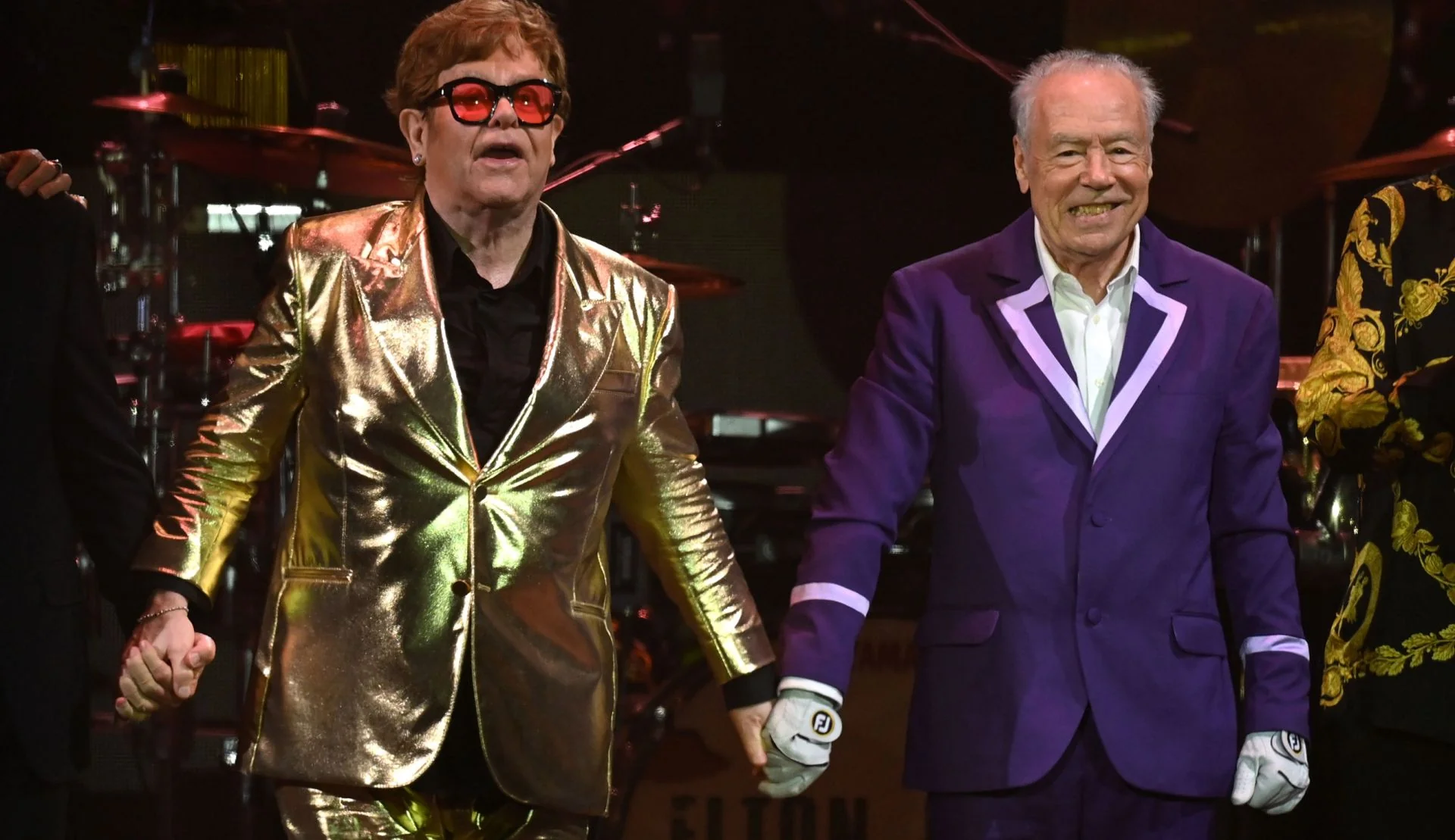 Nigel Olsson on stage with Elton John wearing a purple Tom Cridland suit